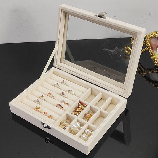Beige jewelry box with mirror lid containing various earrings on a dark surface.