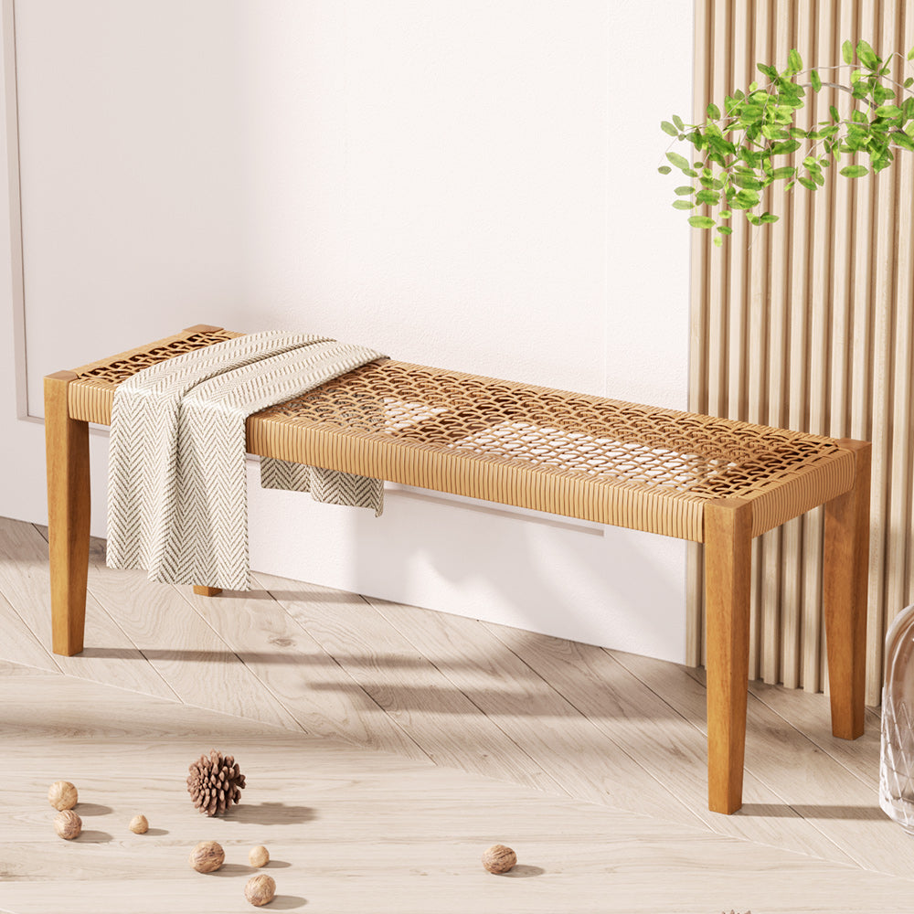 Wooden bench with woven seat in a room with light wood flooring and a plant.